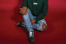 Person wearing a green sweatshirt and ripped jeans sitting on a red floor with 'Oak' branding.